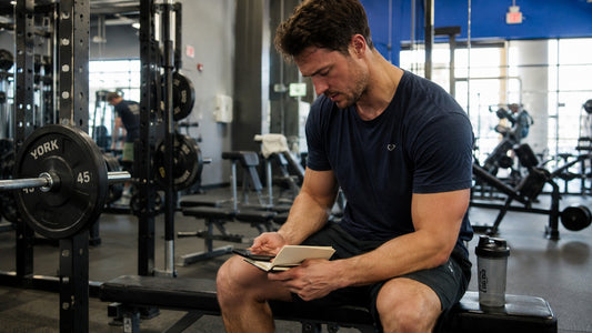 Natural lifter checking weekly training volume in a workout log between sets in a commercial gym